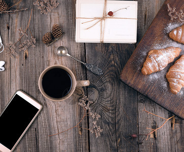 白黑屏幕的智能手机棕色陶瓷杯咖啡和面包喷洒在灰色木本底的冰糖上顶视图片