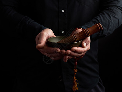 穿黑衬衫的人拿着藏黄铜歌碗和木棍这是冥想祈祷和沉浸在昏睡中的仪式图片