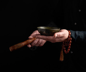 穿黑衬衫的男子在藏铜碗周围旋转木棍冥想祈祷和沉浸在昏睡中的仪式图片