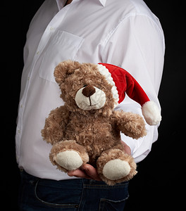 穿白衬衫的男人拿着红帽子的泰迪棕熊圣诞玩具图片