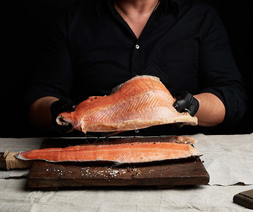 黑衬衫厨师和乳胶手套餐桌上有一大片鲑鱼烹饪过程挤压图片