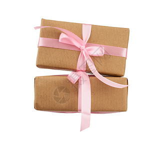 包裹在棕色Kraft纸上并用粉红色丝带捆绑起来的堆叠箱子礼品在白色背景上被隔离设计师的元素图片