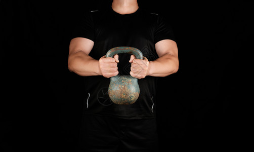 身穿黑色衣服的成年强健运动员在伸展的手臂上用黑色背景握着铁叮当图片