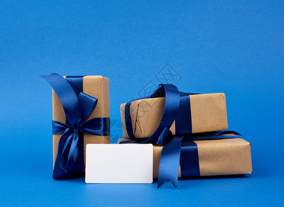 白纸名片和一堆包裹在棕色克拉夫纸上并绑有蓝丝带的盒子礼物放在深蓝色背景上图片
