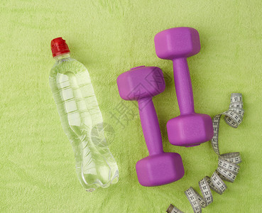 紫色的哑铃和一整瓶清亮的塑料水放在绿色的毛巾上图片