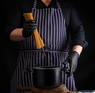 厨师做饭穿黑色乳胶手套的厨师有条纹围裙在锅盘上长着生面条做饭过程背景