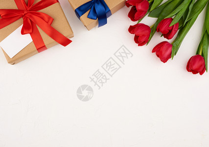 红色盛开的郁金香花束上面有绿色叶子白背景的棕手纸包着礼物复制空间生日情人节的喜悦背景图片