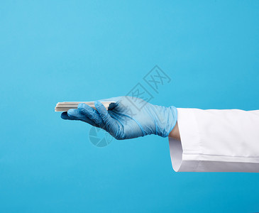 医生用蓝色胶手套在蓝色背景登记地点的空白纸面名片上持有一张空白纸面名片图片