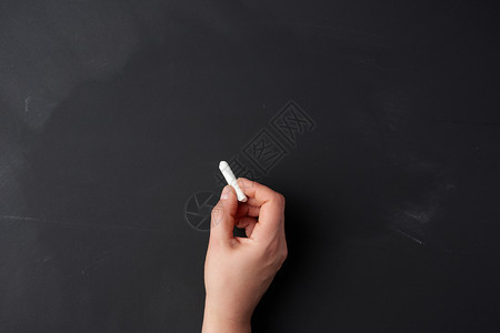 在空黑粉笔板的背景上握着一块白粉笔演示概念回到学校图片