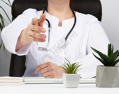 白大衣上的医生坐在桌子上伸出右手握办公室接收病人的概念图片