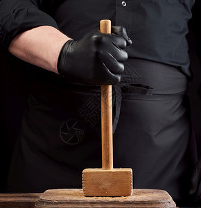 身穿黑衣厨服的师拿着木锤子用黑色背景的旧餐板鞭打肉图片