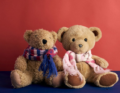 披着围巾的两只泰迪熊坐在红色背景上关图片
