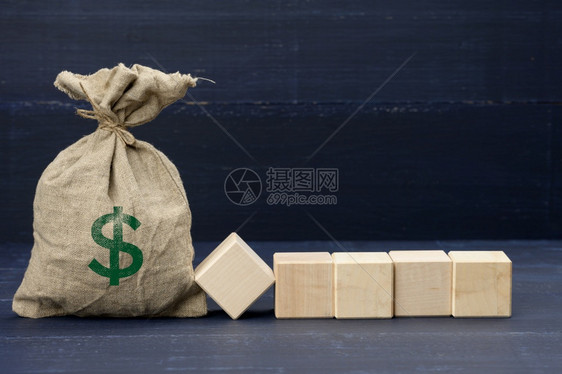 满棕色帆布袋上面有美元图标和5个蓝背景的木形空白方块财富投资补贴和储蓄概念登记地点图片