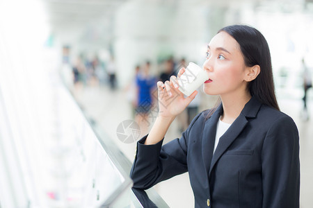 亚洲女商人谈论移动电话并举行咖啡杯反对城市景象商业概念图片