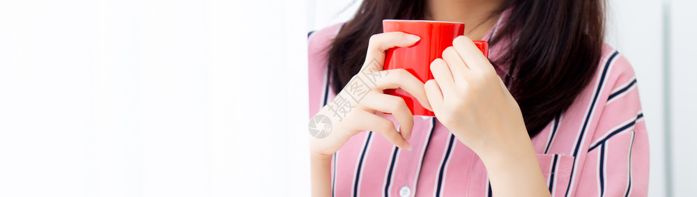 Banner网站美丽的年轻女喝着一杯咖啡站在窗帘边的卧室背景女孩早上在家放松生活方式概念图片