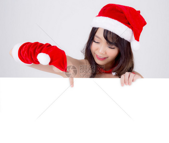 美丽的年轻圣诞老人女子拿着空白板为背景孤立的XmasAsia女孩展示空的标语纸海报并指向圣诞节假日和新年的广告图片