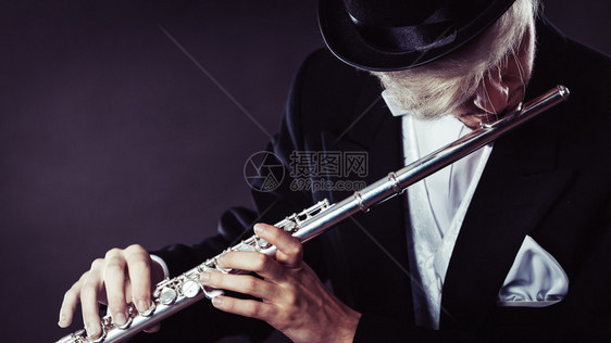 古典音乐激情和业余爱好概念穿着优美服装的音乐人穿着黑色Fedora帽子玩长笛的黑衣音乐人深灰色背景的演播室拍摄穿着优美服装的男音图片