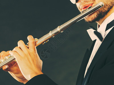 古典音乐激情和业余爱好概念穿着优美服装的音乐人穿着黑色Fedora帽子玩长笛的黑衣音乐人深灰色背景的演播室拍摄穿着优美服装的男音图片