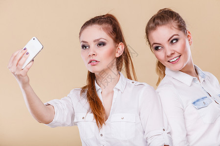 姐妹或最好的朋友两个金发女学生用智能手机相自拍照玩得开心背景图片