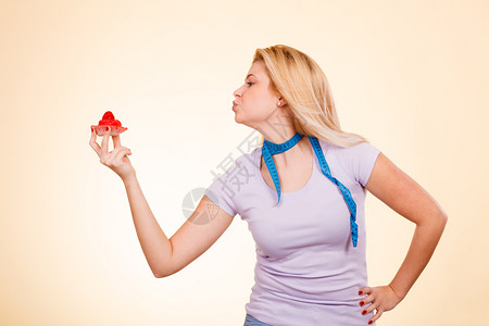 糖果垃圾食品糖诱惑的饮食观念脖子上缠着卷尺的女人手里拿着香甜可口的草莓纸杯蛋糕向甜点送去飞吻拿着卷尺拿着甜蛋糕的女人图片