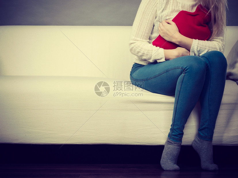 胃痛期和月经抽筋问题概念在可口上坐着肚子抽筋的妇女感觉非常不舒服用热水瓶来感到宽慰在可口乐上坐着肚子抽筋图片