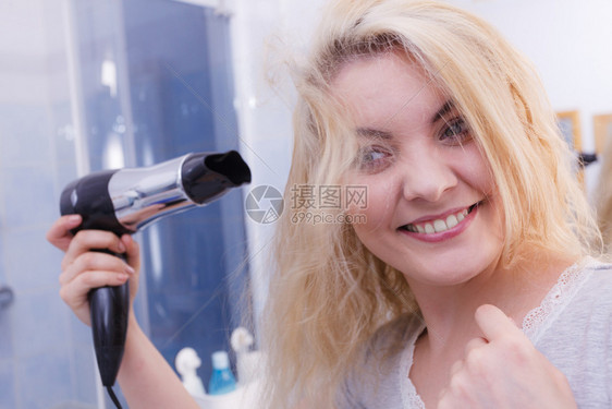 漂亮的长发金女郎在洗手间烘发微笑的女孩手持理发机在湿头吹风妇女在洗手间烘发图片