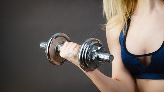 健壮的女举起哑铃重量合适的女孩在锻炼建筑肌肉健身和美在黑暗灰色上合适的女举起哑铃重量图片