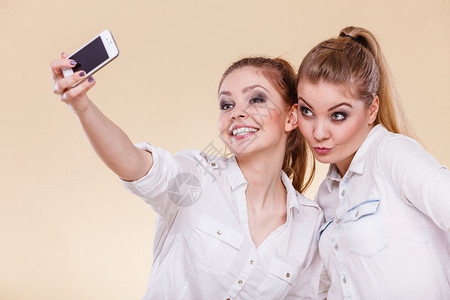 姐妹姊或最好的朋友两个学生金发女孩用智能手机相自拍照背景图片