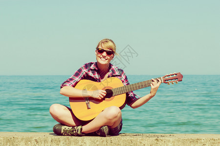 音乐和人的概念年轻女旅行者在海滨露天配吉他图片