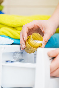 正在洗衣服的人的特写镜头把柔软剂从瓶盖倒进洗衣机里将织物柔软剂倒入洗衣机的人图片