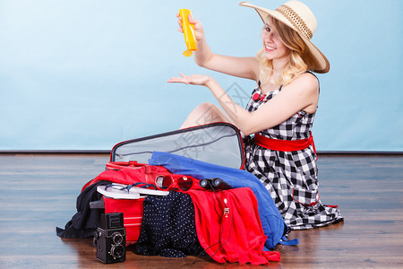 年轻女士坐在地板上拿着手提箱满的东西准备在暑假蓝色的年轻女士包装手提箱背景图片