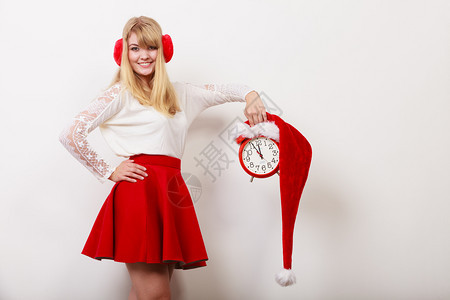 快乐的可爱女人拿着圣达克萨斯帽子的闹钟美丽女孩戴着灰色耳膜圣诞季节概念快乐的女士带着闹钟圣诞时间图片