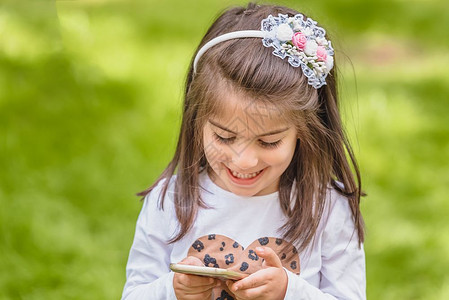 四岁可爱的小女孩穿着临时衣和短信手机在公园户外微笑时图片