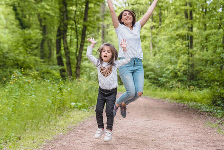 年轻妈和小女孩一起跳跃在快乐的母亲和女儿与爱自然情感的快乐时刻年轻母亲和女儿玩得很开心图片