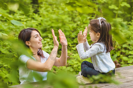 年轻妈和她的小女孩一起在森林中的木板凳上玩得很开心图片