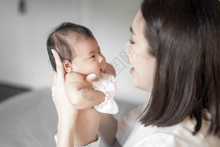 孩子美丽的母亲正在卧室里玩弄她新生的婴儿背景