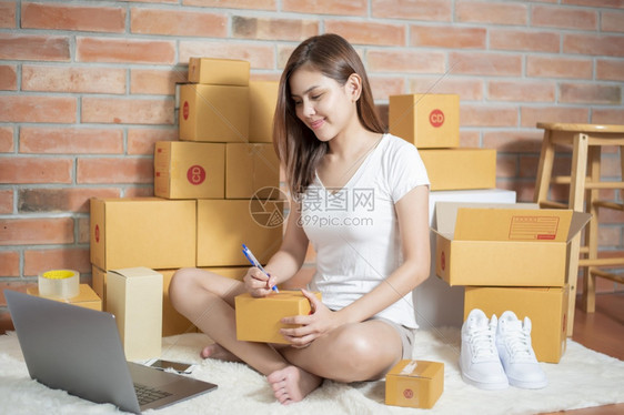 女企业家主中小正在用智能电话膝上型脑和包装箱检查订单以便向其客户发送图片