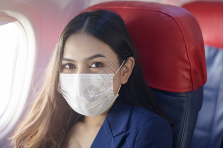 一名年轻女乘客戴着口罩坐在飞机上图片