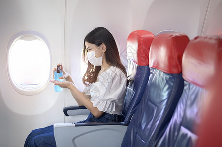 乘客坐在机舱内佩戴着口罩用酒精给手消毒图片