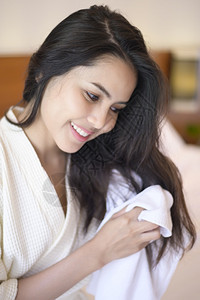 穿着白浴袍微笑的年轻女子在卧室淋浴后用毛巾洗头发图片