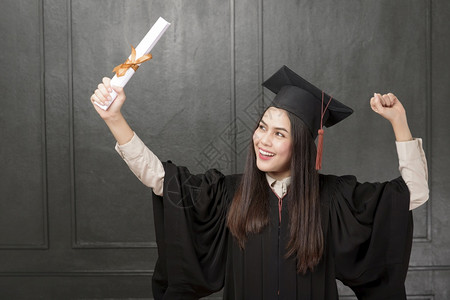 国外学生素材穿着毕业礼服的年轻女子肖像在黑人背景上微笑和欢呼背景