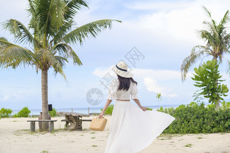 一个穿着白裙子的快乐美丽女人在海滩夏天和节假日享受放松背景