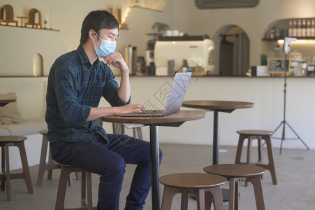 一名在咖啡店用笔记本电脑工作的青年男子身戴面罩的青年男子在咖啡店用笔记本电脑工作身戴19岁和大流行病概念图片