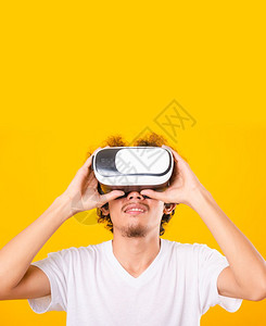 亚洲长着卷发的帅男子使用虚拟现实头耳机或黄色背景的VR玻璃分离器图片