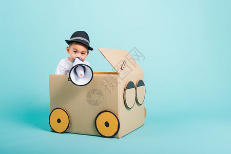 快乐的亚洲儿童男孩笑在驾驶汽车上由纸板盒想象力制作有扩音器暑假旅行概念蓝背景摄影棚拍复制文本空间图片