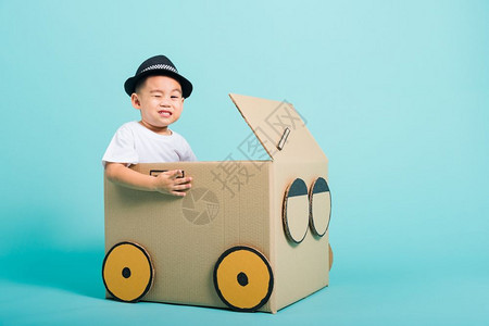 快乐的亚洲儿童男孩在驾驶车时微笑由纸箱想象力暑假旅行概念蓝背景摄影棚拍图片