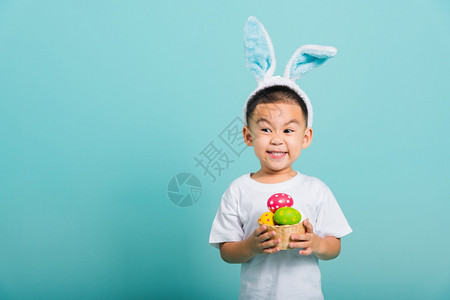 亚洲可爱的小孩男微笑带着兔子耳朵和白色T恤衫站在篮子上着背景图片