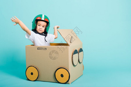 快乐的亚洲儿童男孩在驾驶汽车时笑着Helmet的Helmet亚洲男孩由纸板盒想象力暑假旅行概念蓝背景摄影棚拍复制文本空间图片