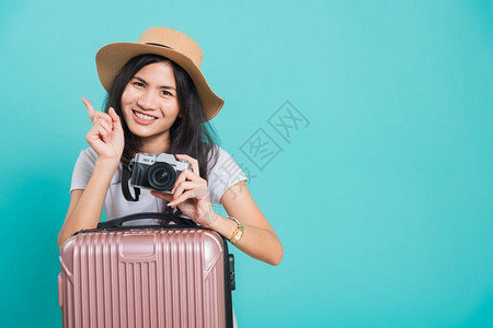 旅行者快乐的亚洲年轻美女穿着白色T恤衫假期旅行概念她拿着李袋照片不摄影机在棚拍蓝底照片图片