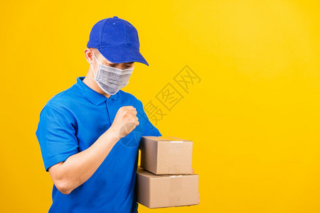 身穿蓝色T恤衫和帽子制服的亚洲年轻送货工人身穿蓝色T恤衫和帽子制服的亚洲年轻送货员身着面罩在服务客户使用科罗纳或COVID19服背景图片